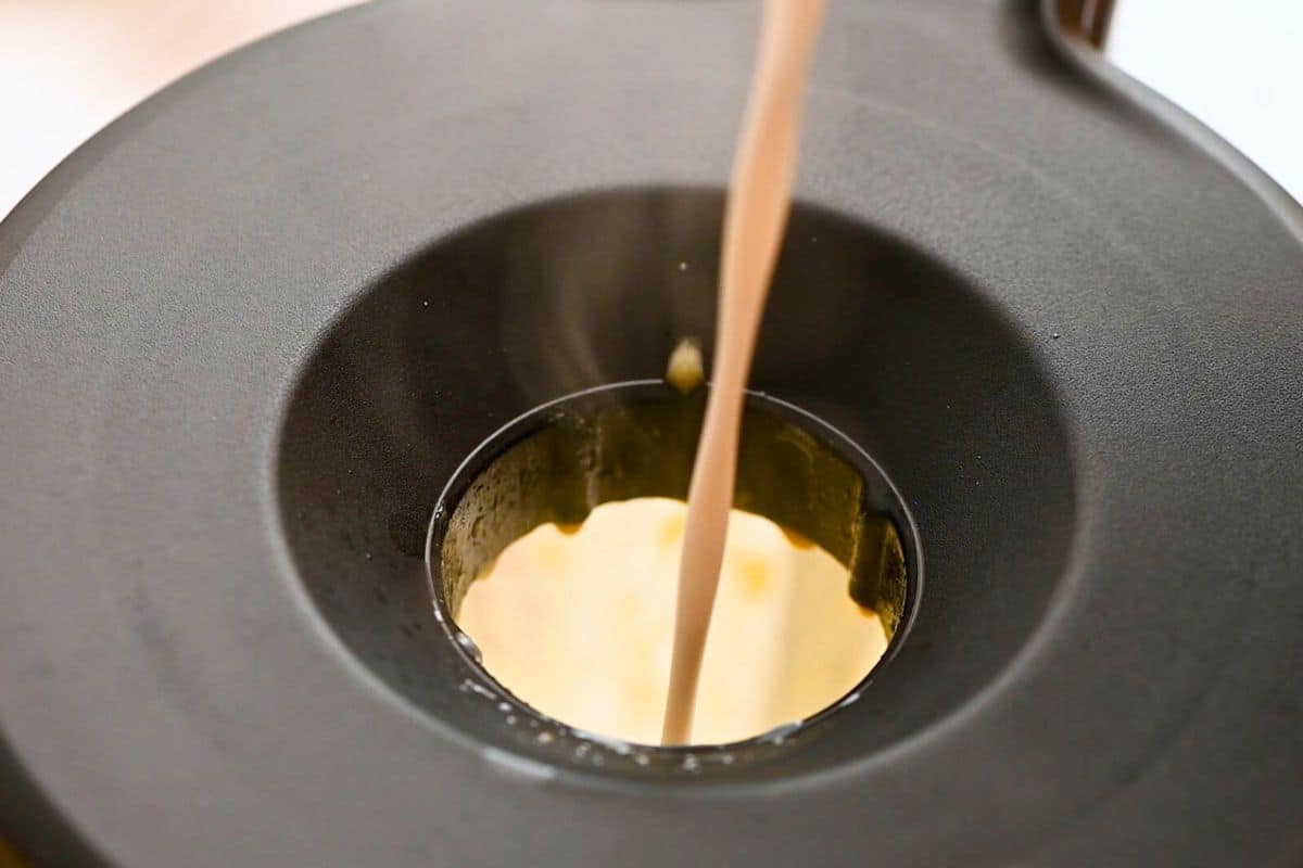 homemade dairy-free eggnog Warmed coconut milk being drizzled in steady stream through opening on blender to make homemade dairy-free eggnog.