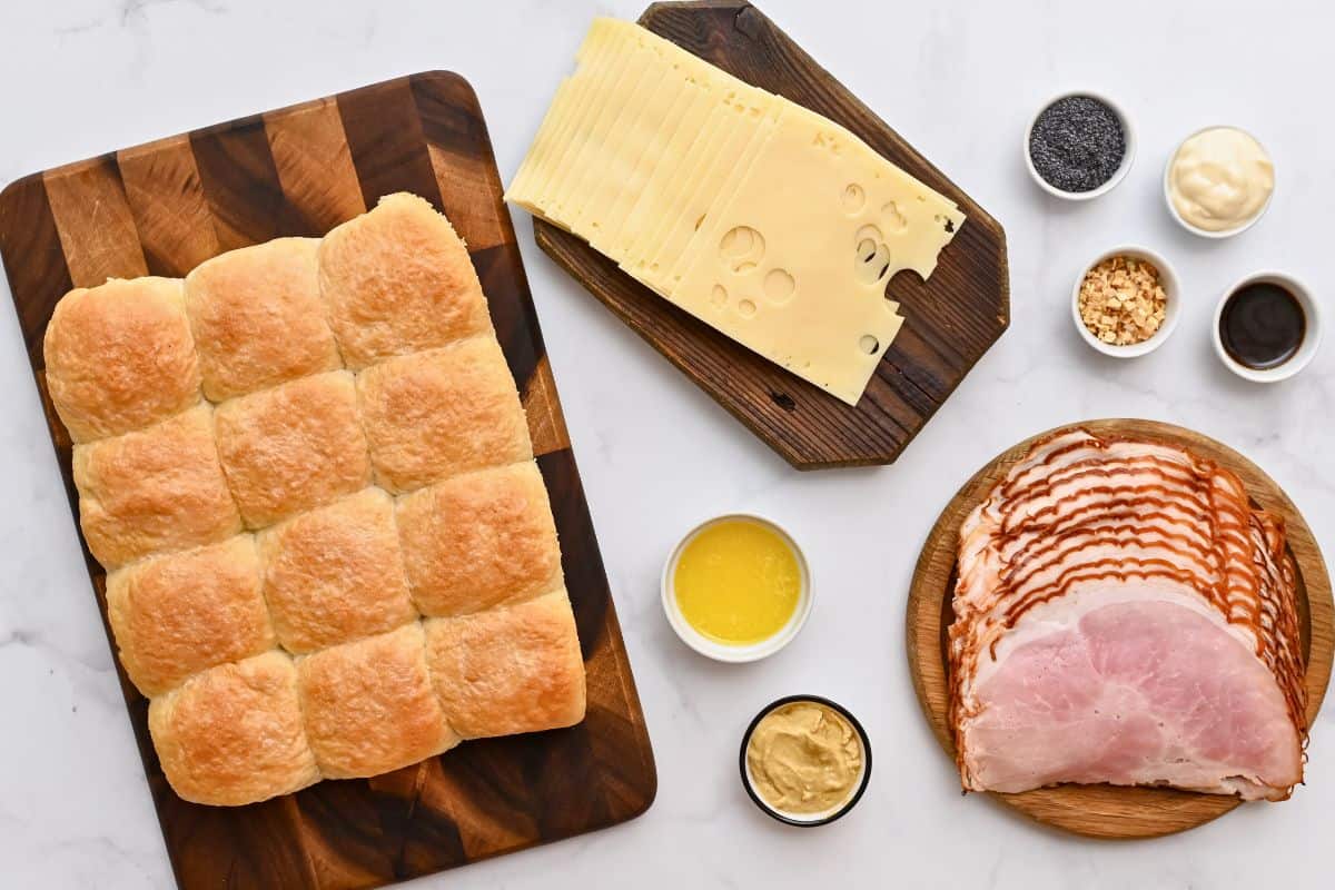 Recipe Ham and Cheese Sliders Slider rolls, deli ham, Swiss cheese slices, melted butter, Dijon, mayonnaise, poppy seeds, onion flakes, and Worcestershire sauce on counter.