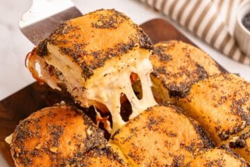 Ham and Cheese Slider being pulled from baked tray of sliders to show melted cheese pull.