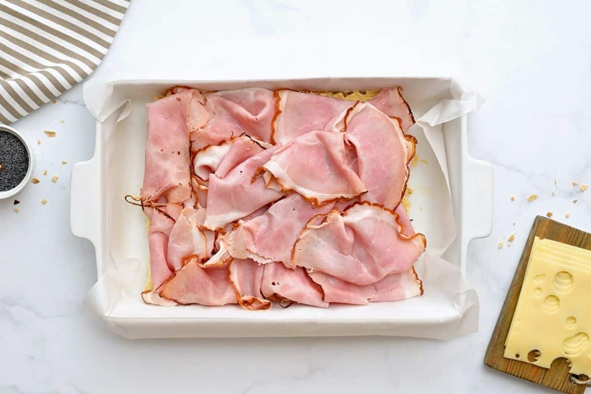 Hawaiian Ham Cheese Sliders Hawaiian rolls with mustard in baking dish topped with thinly sliced deli ham.