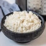 Fluffy white rice that was cooked in instant pot in black bowl with Instant Pot in background.