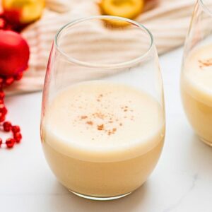 Homemade dairy free eggnog made with coconut milk in a glass mug sprinkled with grated nutmeg next to Christmas ornaments.