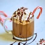 Peppermint mocha in glass mug drizzled with chocolate syrup and crushed peppermint canes.