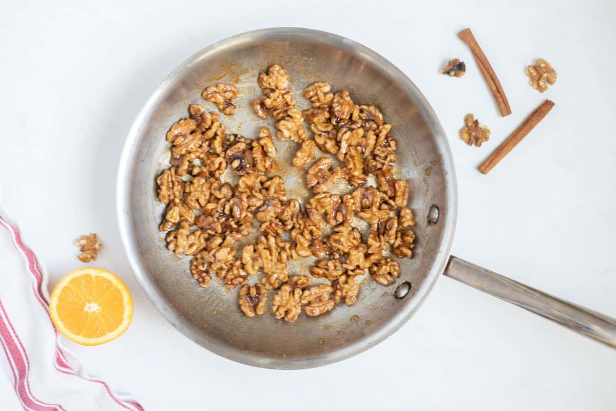 Walnuts coated with orange juice, orange zest, brown sugar, white sugar, cinnamon, salt, and cayenne in stainless steel skillet.