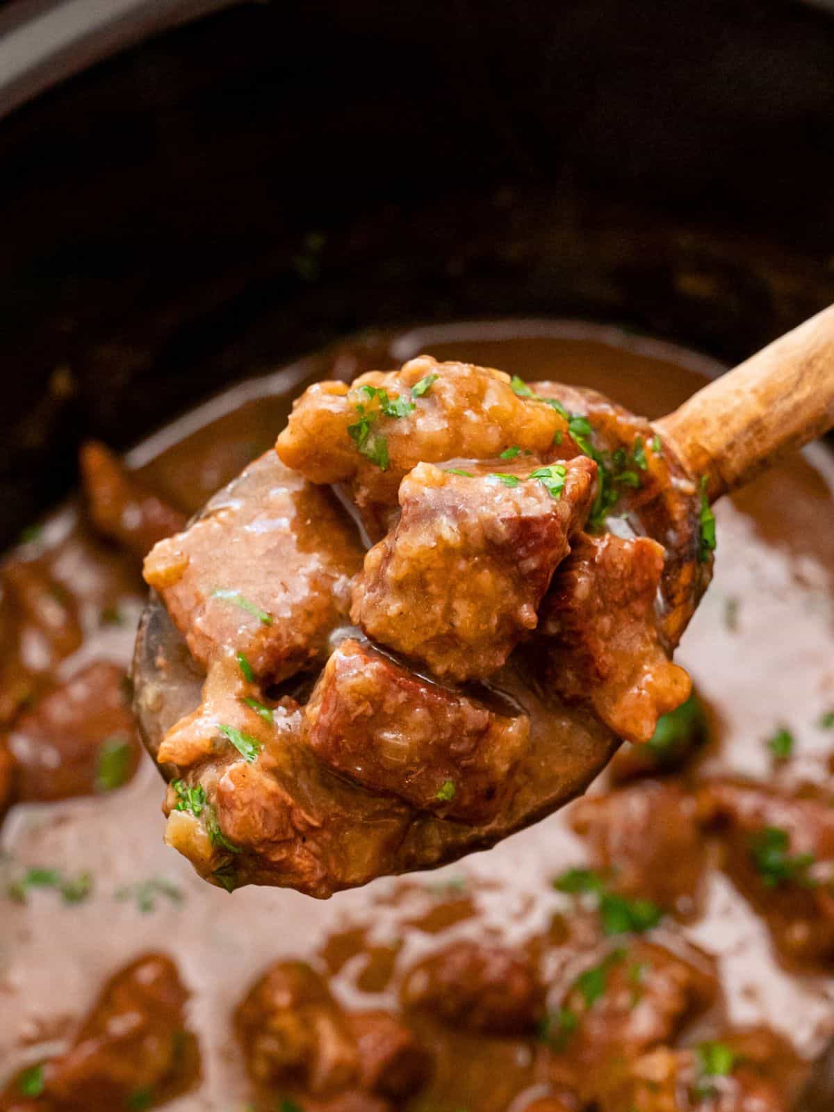 Scooping out beef tips from crock pot with rich glossy gravy.