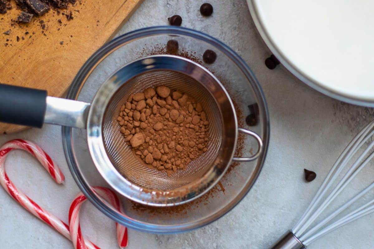 How to make homemade hot chocolate Cocoa powder being sifted through fine mesh strainer for base of homemade hot chocolate.