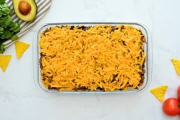 Corn chips, taco meat, beans, corn, and cheese layered in 7x11 baking dish before baking.