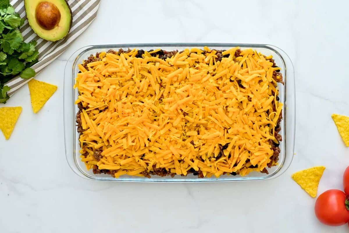 Easy Taco Casserole Recipe Corn chips, taco meat, beans, corn, and cheese layered in 7x11 baking dish before baking.