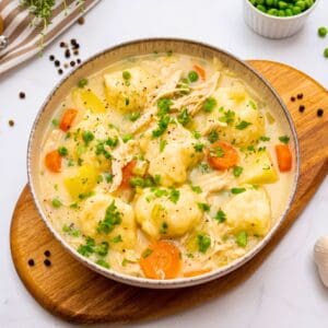 Bowl of creamy soup with shredded chicken, cooked carrots, potatoes, peas and homemade dumplings.