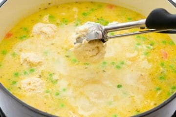 Small cookie scoop dropping homemade dumpling dough into simmering homemade chicken soup.