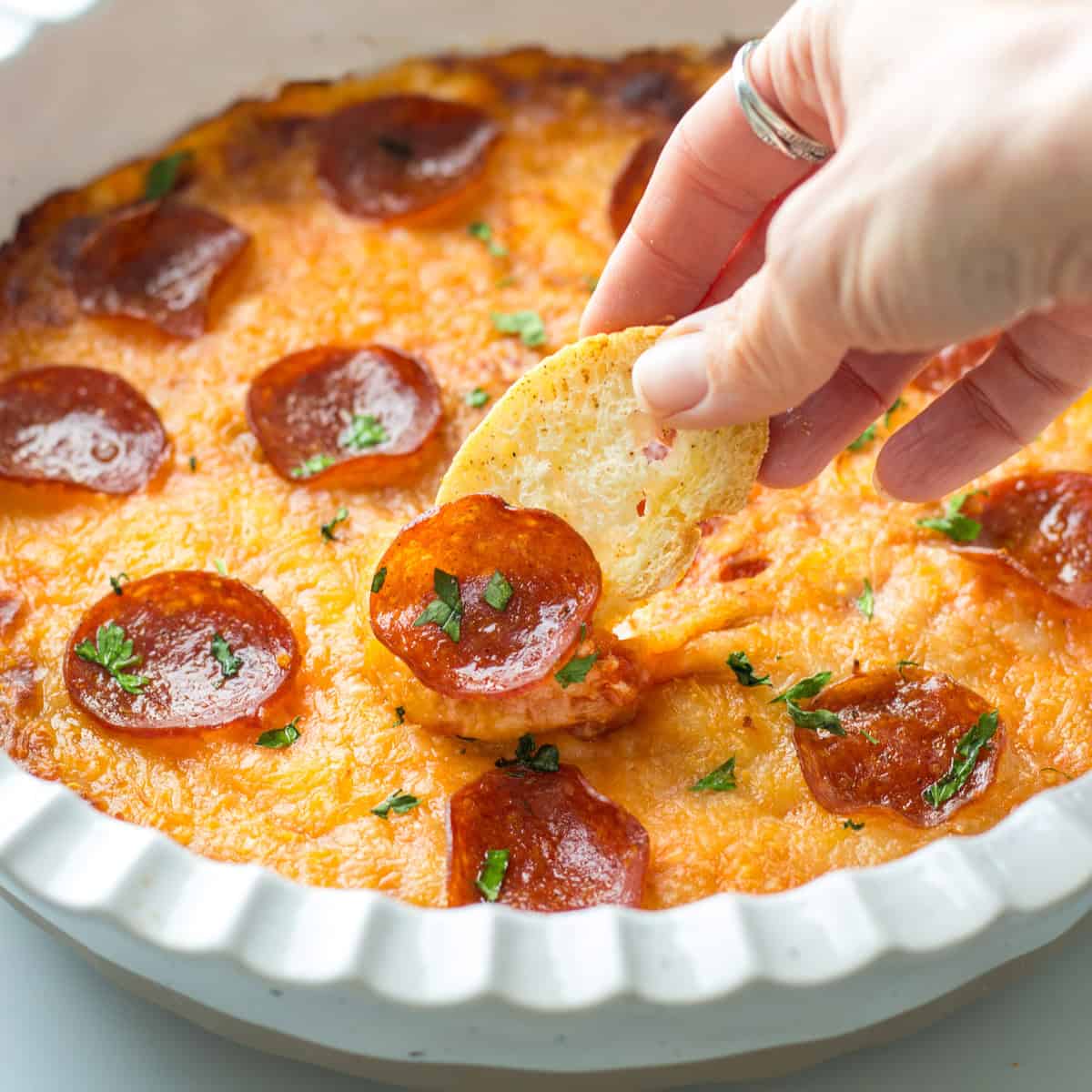 Game Day Party Food Ideas Baked Pizza dip topped with pepperoni and toasted crostini dipping into the cheesy dip.