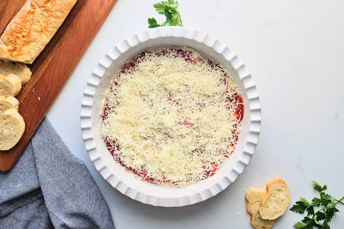 Pizza Dip Recipe with Pepperoni Cream cheese and cottage cheese based spread out in shallow layer in pie plate topped with pizza sauce, and shredded mozzarella cheese