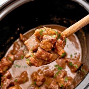 Spoonful of beef tips with gravy coming out of crockpot after being slow cooked.