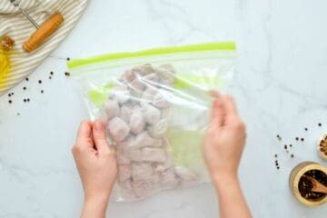 Cubes of beef and flour and seasonings in large storage bag being shook to coat beef.