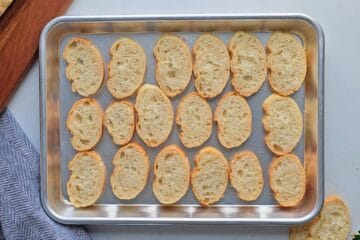 Sliced baguette on baking tray after being lightly toasted to serve with pizza dip.