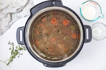 Broth, wild rice, sauteed veggies and herbs for wild rice soup layered inside Inner pot of pressure cooker before pressure cooking.