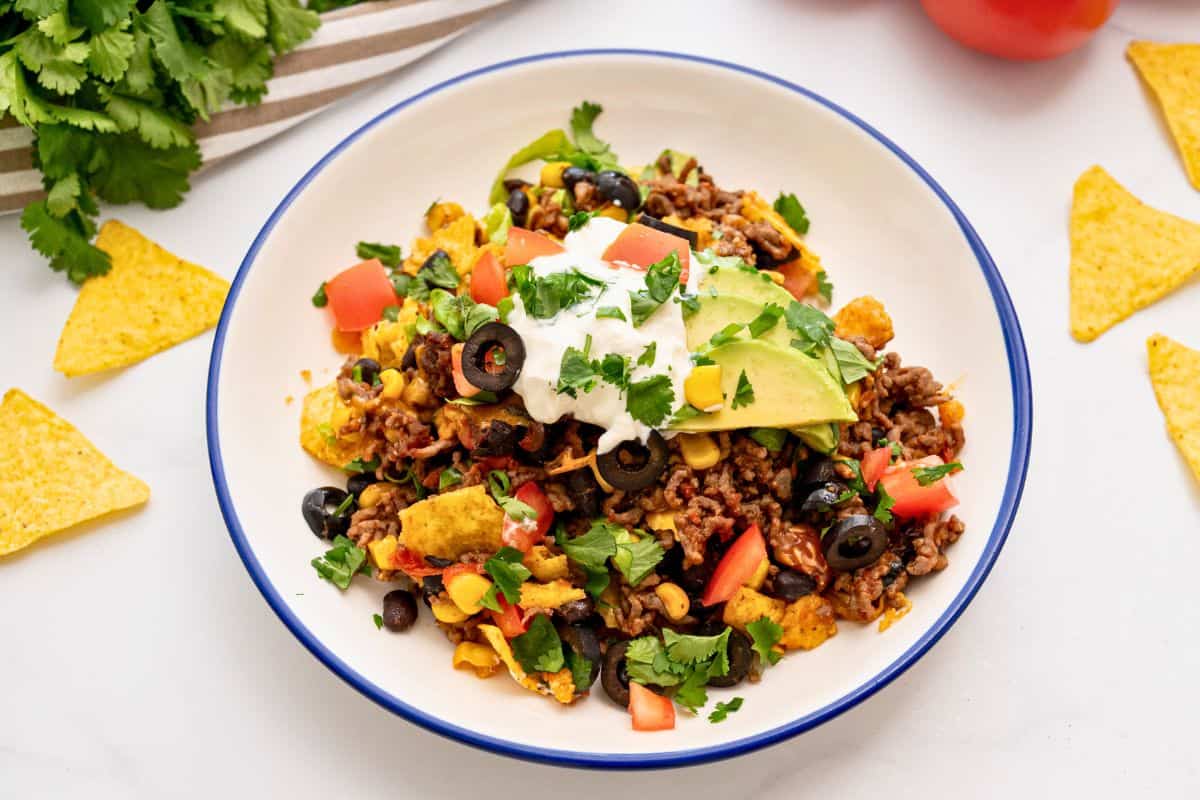 Plate of taco casserole made with ground beef and beans, cheese topped with lettuce, cilantro, tomatoes, and sliced avocado.