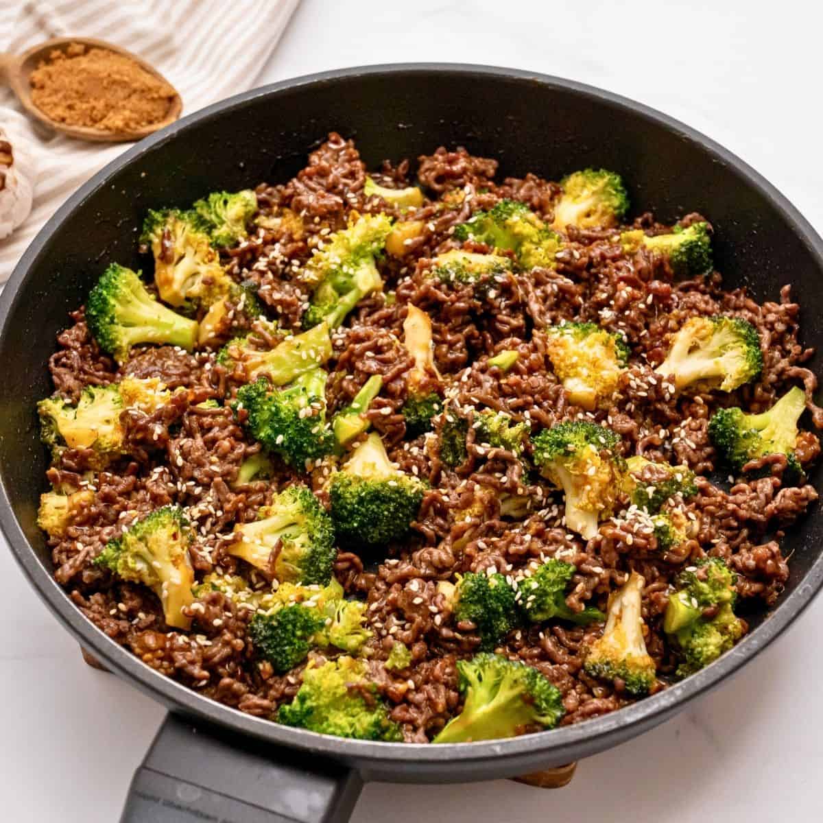 Fast Stir Fry recipes for busy nights Ground beef with broccoli stir fry in pan topped with sesame seeds.