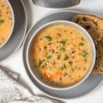 Bowl of creamy vegetarian Instant Pot Wild Rice Soup in grey bowl topped with parsley served with hearty bread.