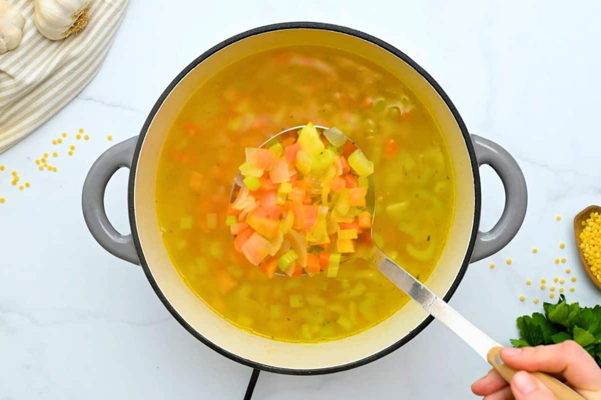 Italian Penicillin Recipe Ladle of carrots, celery and onions coming out of soup pot.