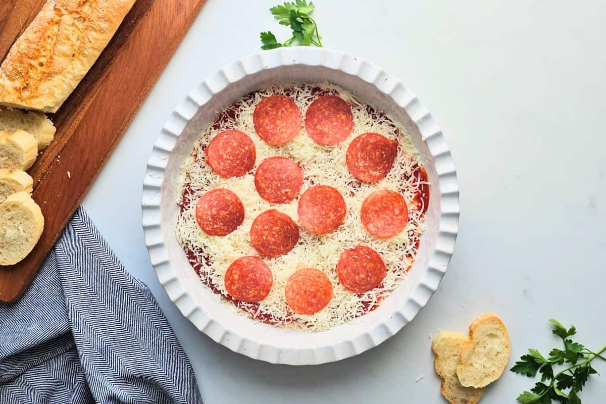 Pepperoni Pizza Dip Cream cheese and cottage cheese based spread out in shallow layer in pie plate topped with pizza sauce, shredded mozzarella cheese, and sliced pepperoni.