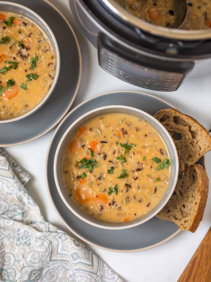 Two bowls of Instant Pot Wild Rice Soup in grey bowls topped with parsley served with hearty bread with Instant Pot in background.
