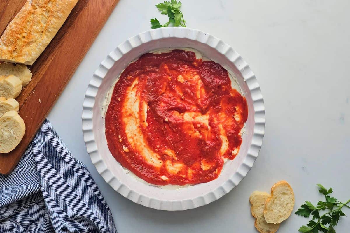 Pizza Dip Recipe Cream cheese and cottage cheese based spread out in shallow layer in pie plate topped with pizza sauce.