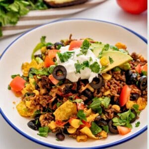 Plate of taco casserole made with ground beef and beans, cheese topped with lettuce, cilantro, tomatoes, and sour cream.