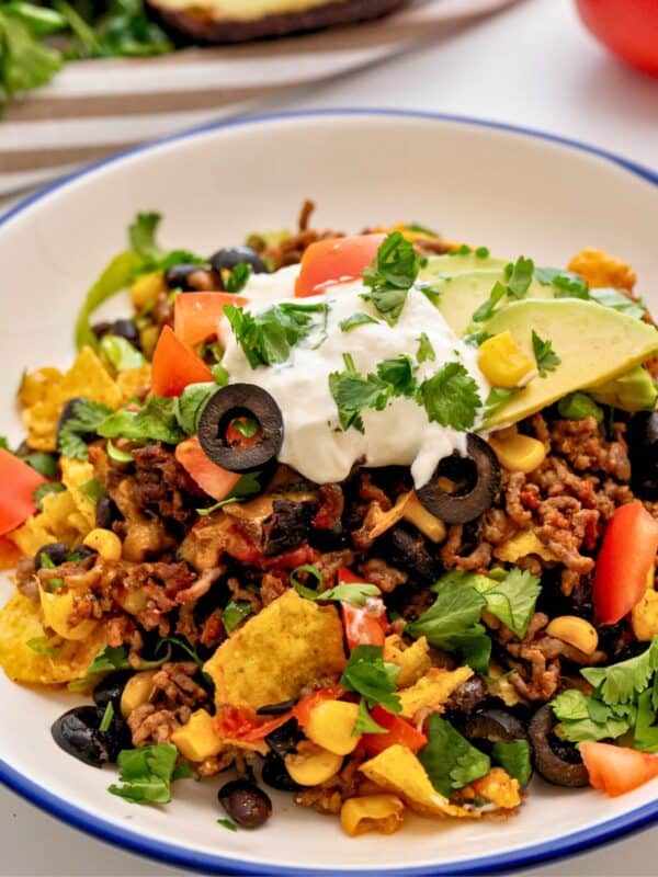 Plate of taco casserole made with ground beef and beans, cheese topped with lettuce, cilantro, tomatoes, and sour cream.
