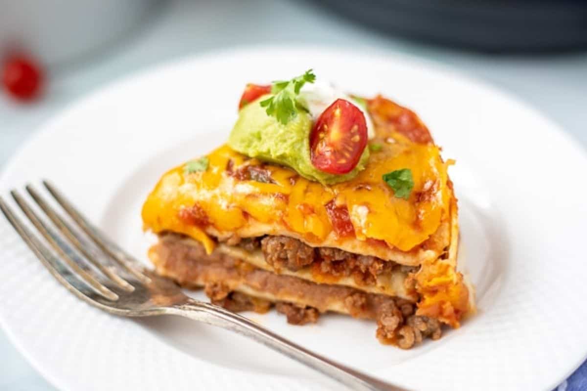 Instant Pot Dinner Ideas Slice of Instant Pot Taco Lasagna on white plate topped with tomato and guacamole.