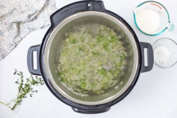 Softened diced yellow onions and celery inside inner pot of Instant Pot for base of Instant Pot Wild Rice Soup.