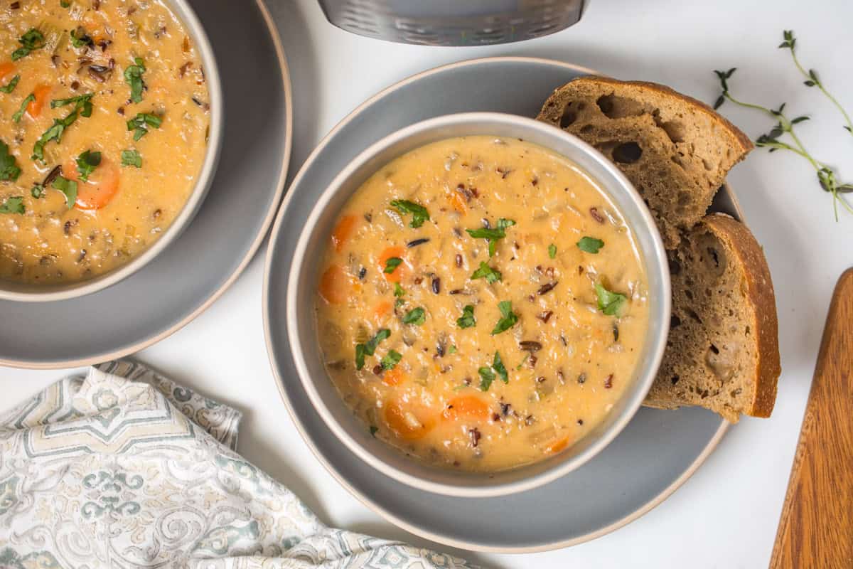 Recipe Instant Pot Wild Rice Soup Two bowls of Instant Pot Wild Rice Soup in grey bowls topped with parsley served with hearty bread with Instant Pot in background.