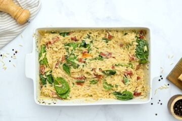 Orzo in baking dish with spinach stirred into it.
