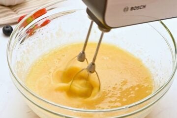 Handheld mixer beating eggs, sour cream, sugar, and oil together.