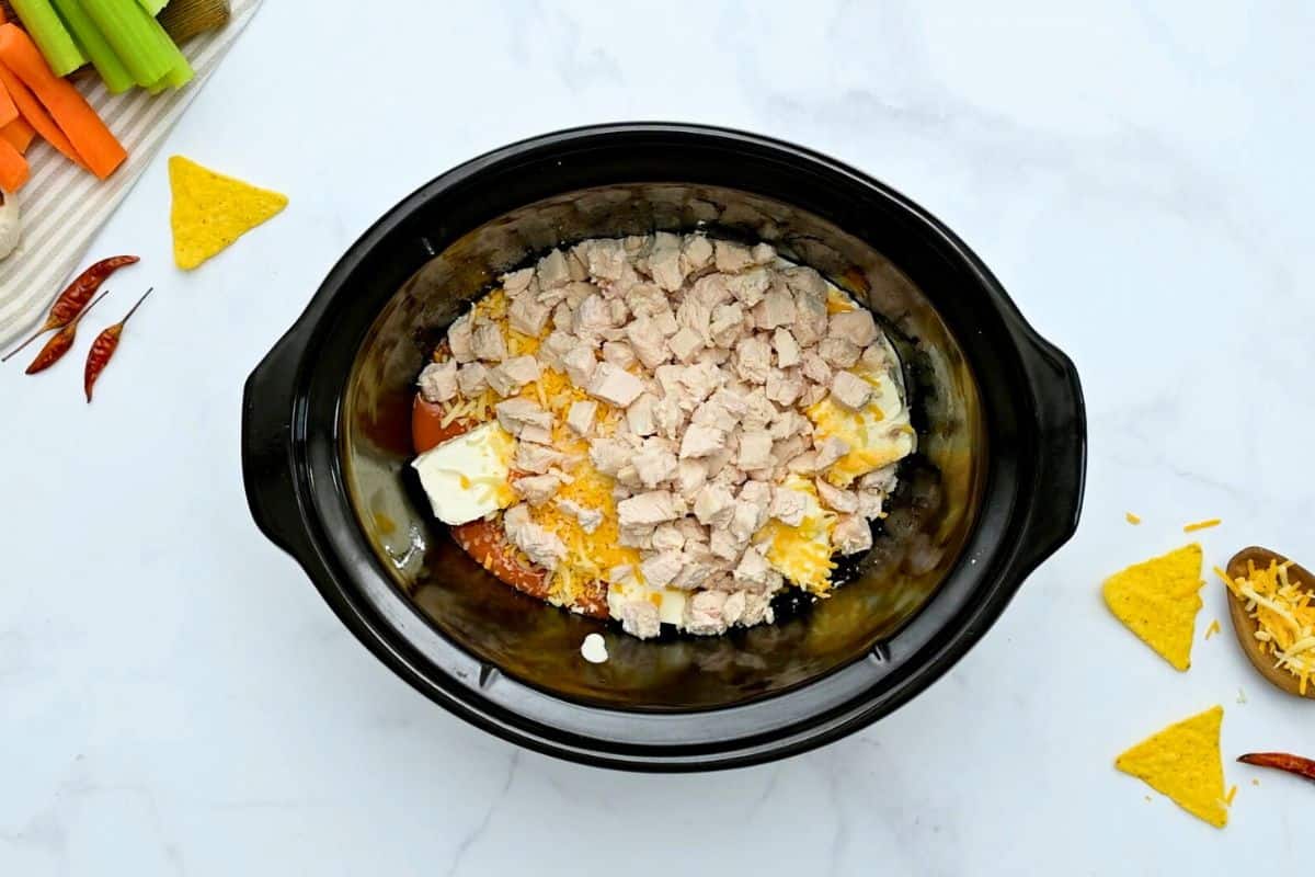 Slow Cooker Chicken Wing Dip Cubed cream cheese, ranch dressing, shredded cheese, garlic powder, hot wing sauce, and diced chicken inside the slow cooker.