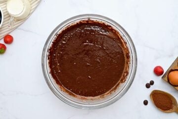 Cake batter for chocolate bundt cake in mixing bowl with cocoa powder on the side.