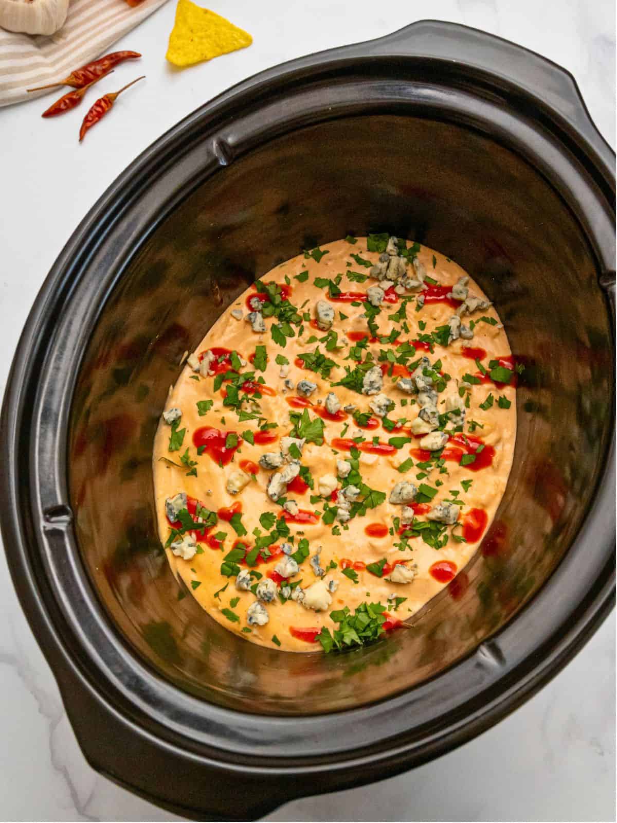 Buffalo Wing Dip Cheesy crockpot buffalo dip inside crockpot topped with hot sauce, cilantro, and bleu cheese crumbles.