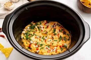 Creamy, cheesy dip made with cream cheese, buffalo sauce, cream cheese, and chicken inside inner pot topped with buffalo sauce, cilantro, and bleu cheese.