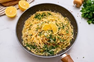 Pasta tossed with lemon, garlic butter, and parmesan in skillet topped with lemon slices and fresh minced parsley.