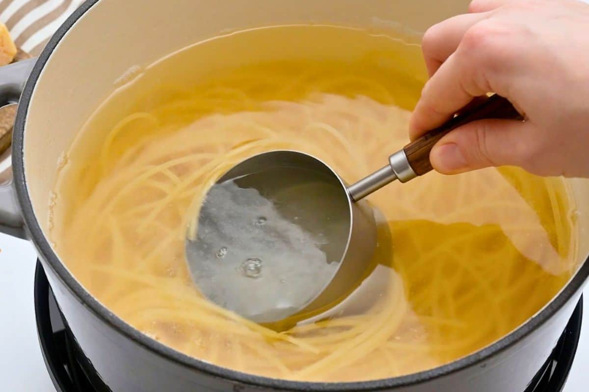 Recipe Lemon Pasta Measuring cup scooping out cooking water from spaghetti cooking in large pot.