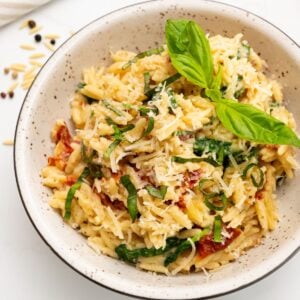 Bowl of marry me orzo with sun-dried tomatoes and spinach served in bowl topped with basil and parmesan.
