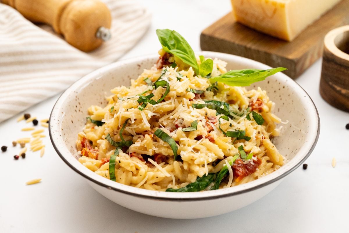 Parmesan Baked Orzo Bowl of baked orzo with sun-dried tomatoes and spinach served in bowl topped with basil.