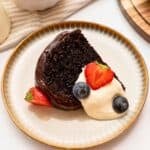 Slice of sour cream chocolate bundt cake iced with ganache topping on plate with berries and whipped cream.