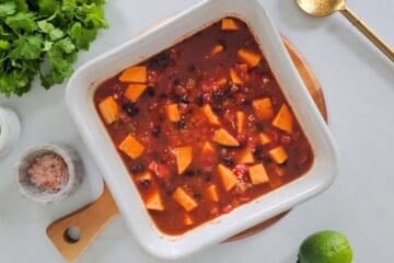 Quinoa with cubed sweet potatoes, canned black beans, diced tomatoes, vegetable broth, and taco seasoning in white dish before baking.