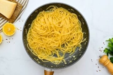 Cooked spaghetti tossed with garlic butter in skillet.