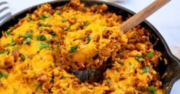 Spoonful of taco rice casserole made with rice, beef, beans, and cheese coming out of deep skillet.