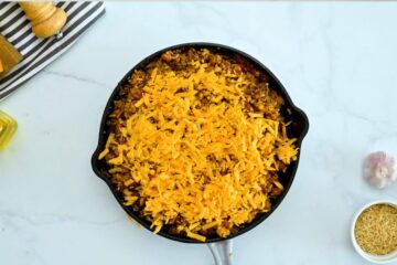 Baked taco rice casserole in deep skillet topped with shredded cheddar.