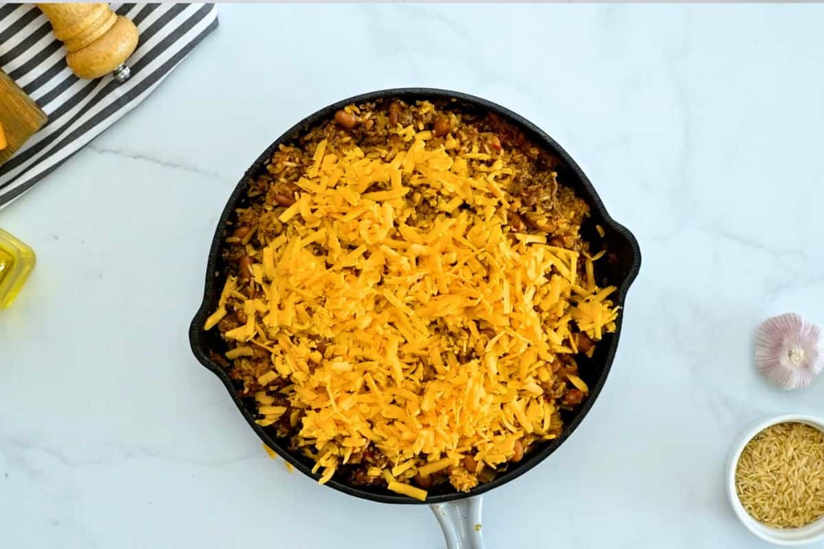 Taco Rice Baked Baked taco rice casserole in deep skillet topped with shredded cheddar.