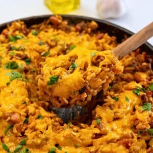 Spoon scooping out baked taco seasoned rice with beef and beans from skillet.
