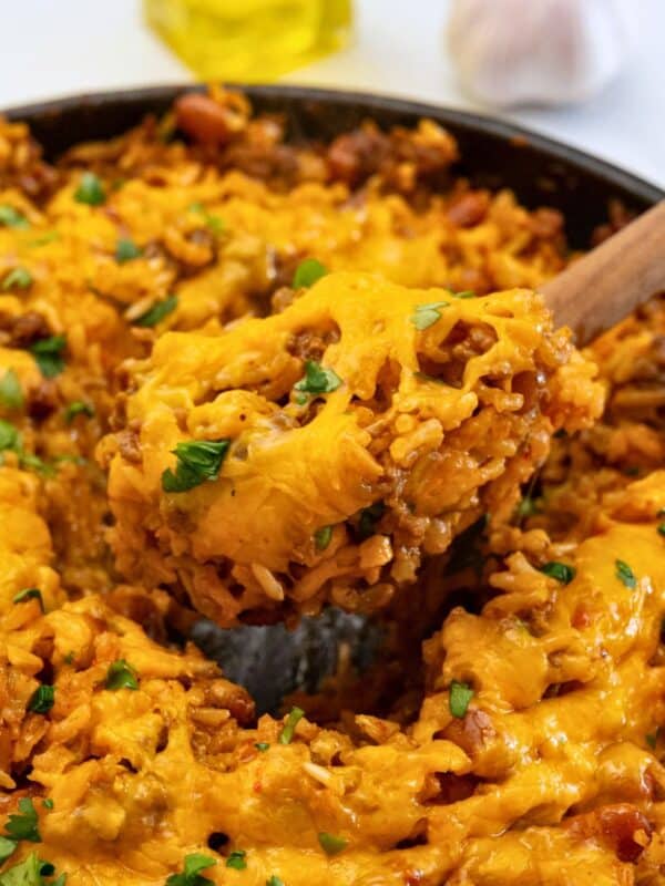 Spoon scooping out baked taco seasoned rice with beef and beans from skillet.